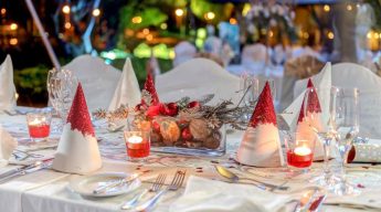 Festive table setting featuring red and white cone-shaped napkin decorations, candles, and a central arrangement of pine cones and berries, creating a vibrant, celebratory atmosphere.