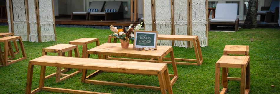 Henna station setup for wedding or event with low wooden benches, tables, and macrame bohemian room dividers on a lawn.