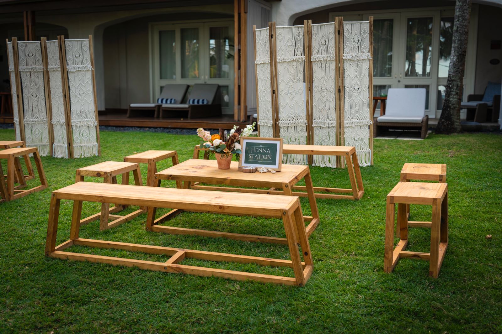 Henna station setup for wedding or event with low wooden benches, tables, and macrame bohemian room dividers on a lawn.