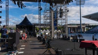 Wide shot of a large outdoor concert stage and scaffolding being set up under a blue, cloudy sky before an event.