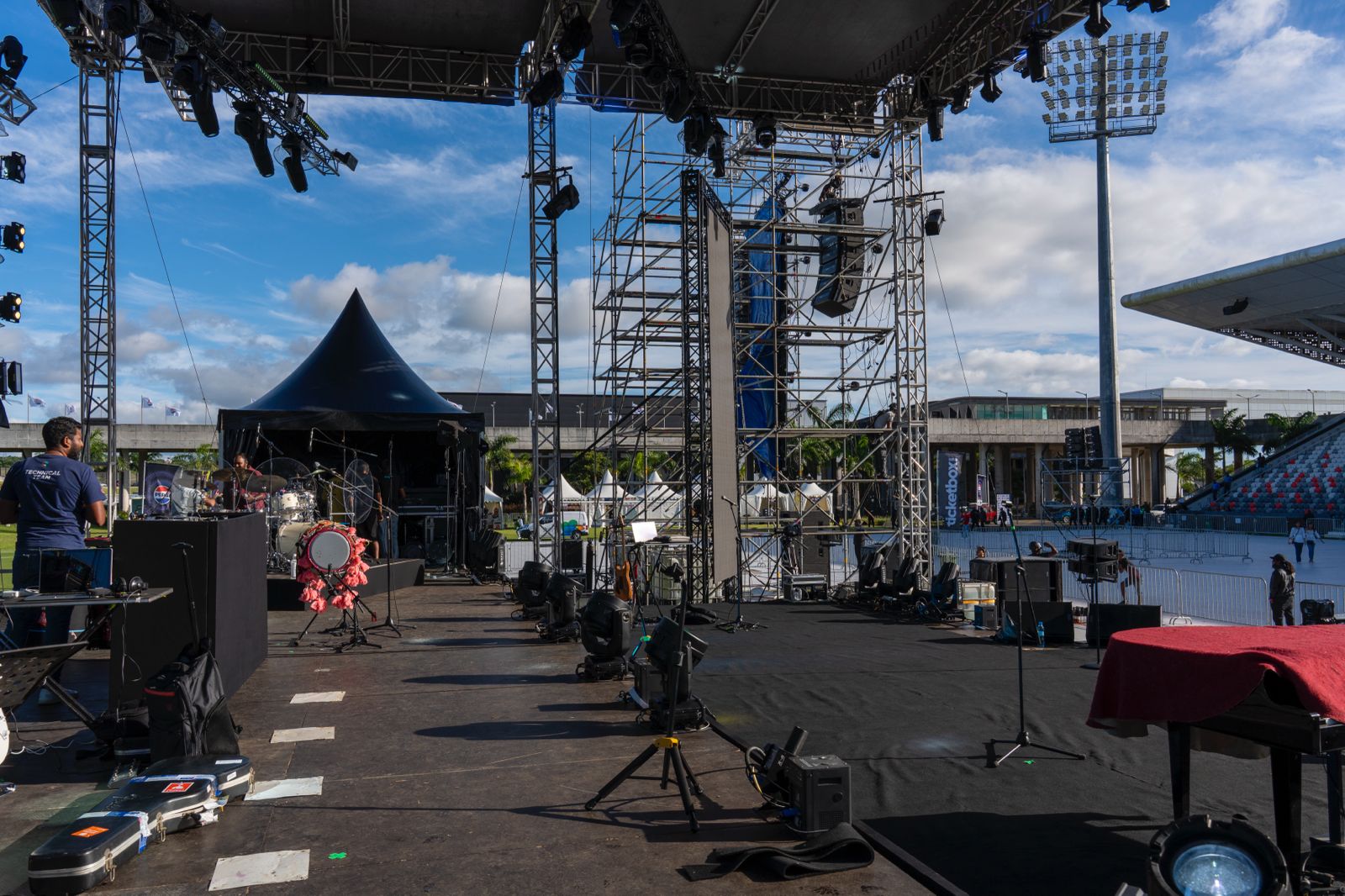 Wide shot of a large outdoor concert stage and scaffolding being set up under a blue, cloudy sky before an event.