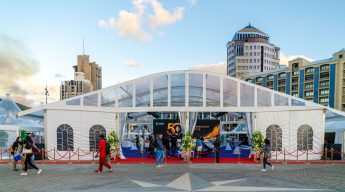 A large white event tent with a clear roof structure, set up in an urban square with a star pattern on the ground and modern high-rise buildings in the background, showing people entering the tent on a red carpet.