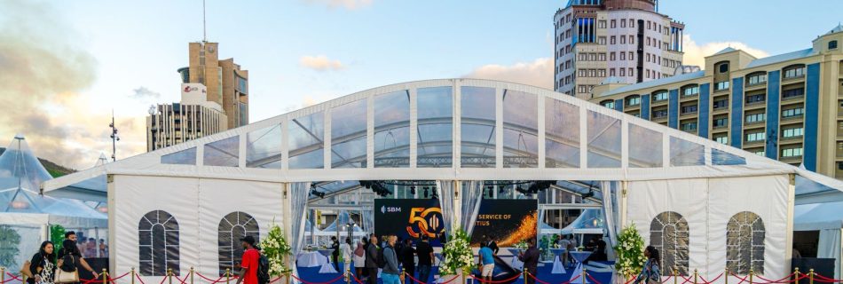 A large white event tent with a clear roof structure, set up in an urban square with a star pattern on the ground and modern high-rise buildings in the background, showing people entering the tent on a red carpet.