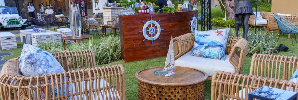 Daytime view of an outdoor lounge area with woven rattan chairs, a wood ship-themed bar, and nautical-themed pillows and decorations.