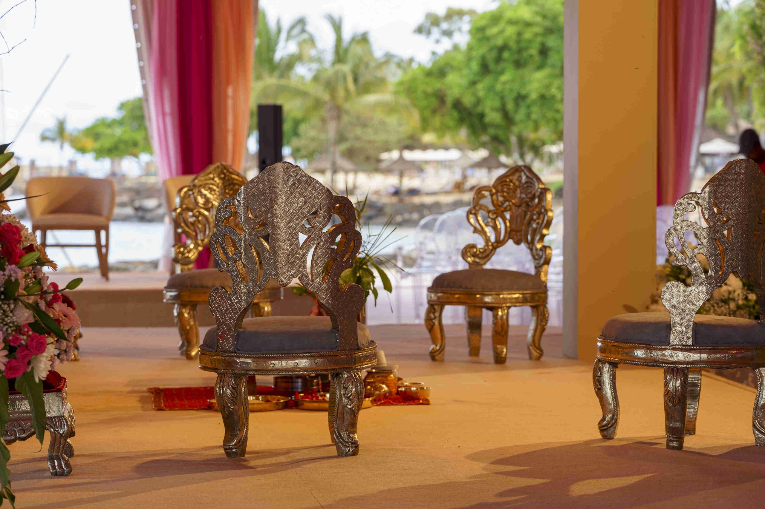 Elegant chairs with ornate silver designs are arranged on a stage with tropical plants in the background. The setting is luxurious and ceremonial.