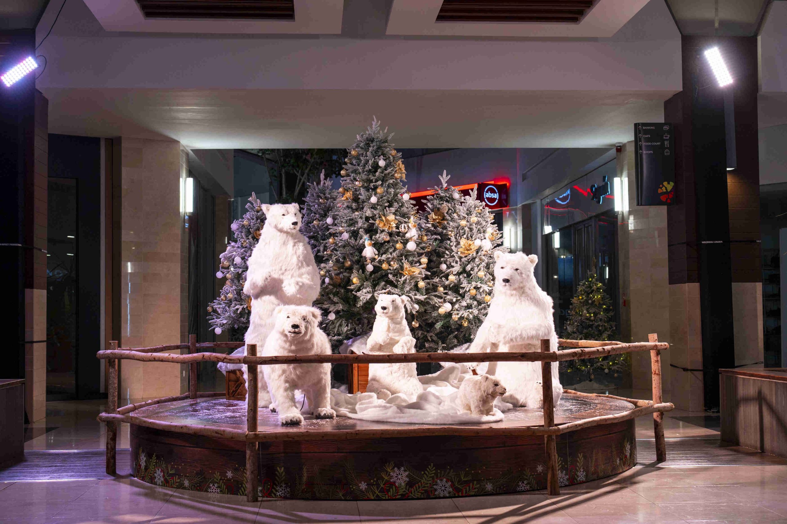 Festive polar bear display with life-sized bear figures around a decorated Christmas tree, set on a wooden platform. Warm lighting creates a cozy, joyful ambiance.