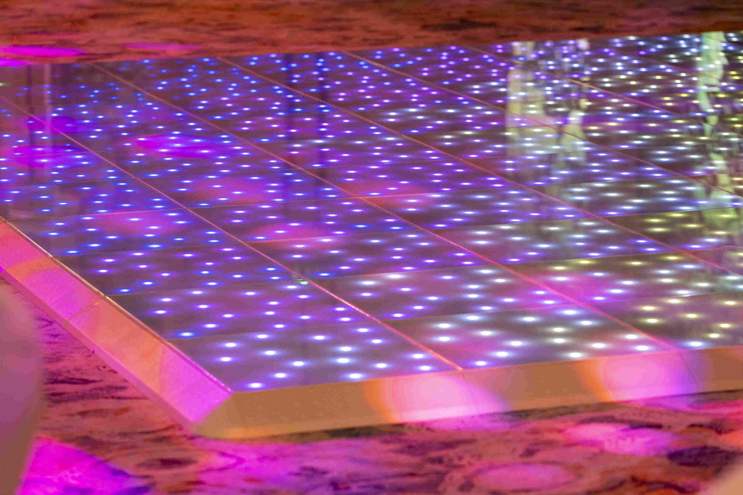 Sparkling LED dance floor with a grid pattern emits vibrant blue and pink lights, creating a lively and festive atmosphere.