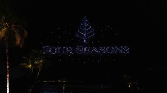 Night scene with "Four Seasons" written in bright lights above a palm tree by a reflective water surface. The atmosphere is serene and elegant.