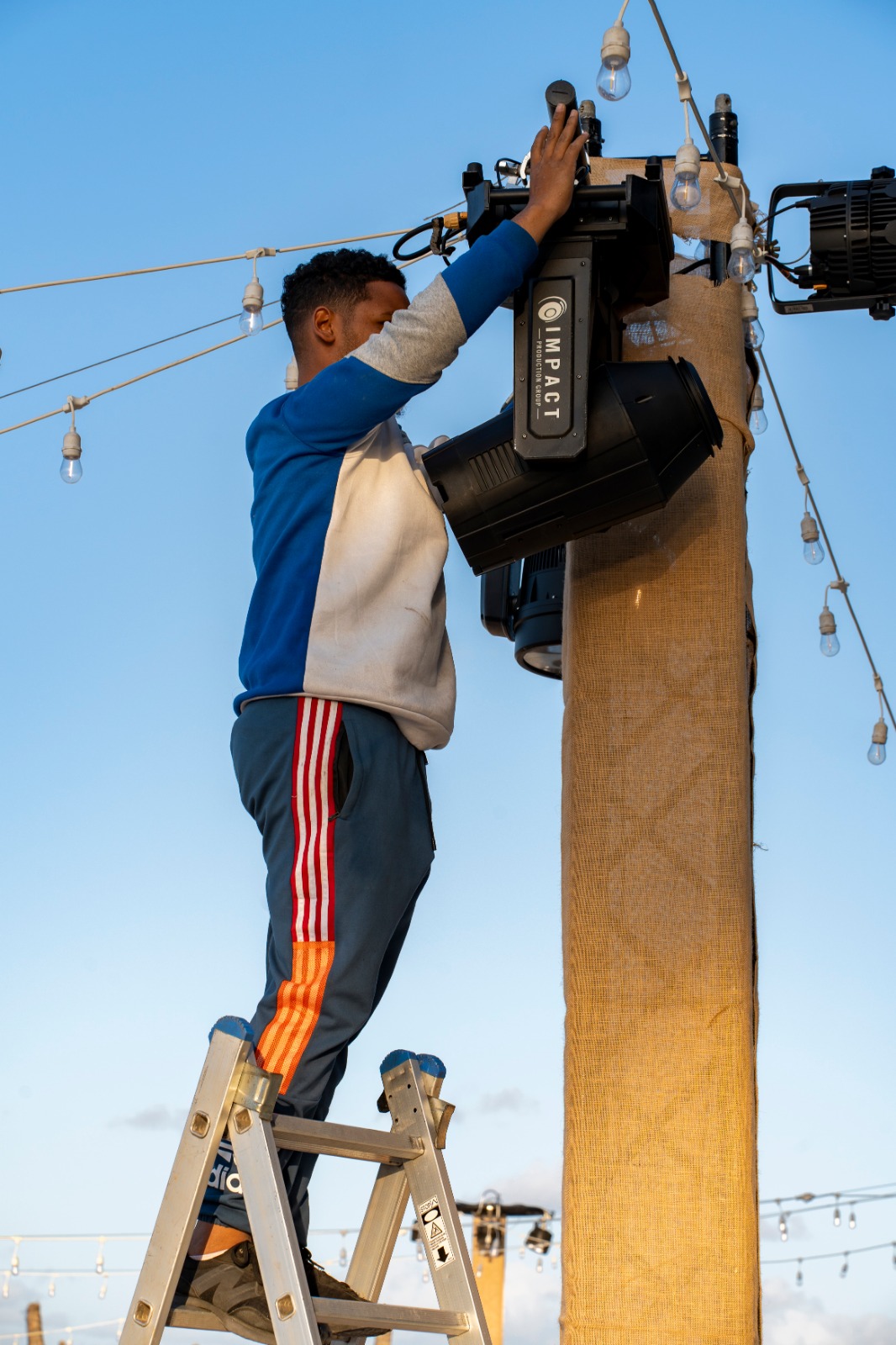 person-adjusting-stage-light-ladder-wooden-pole-string-lights