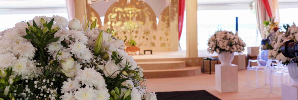 Elegant wedding venue with pink and white drapes, white floral arrangements, and a gold backdrop. The atmosphere is celebratory and stylish.