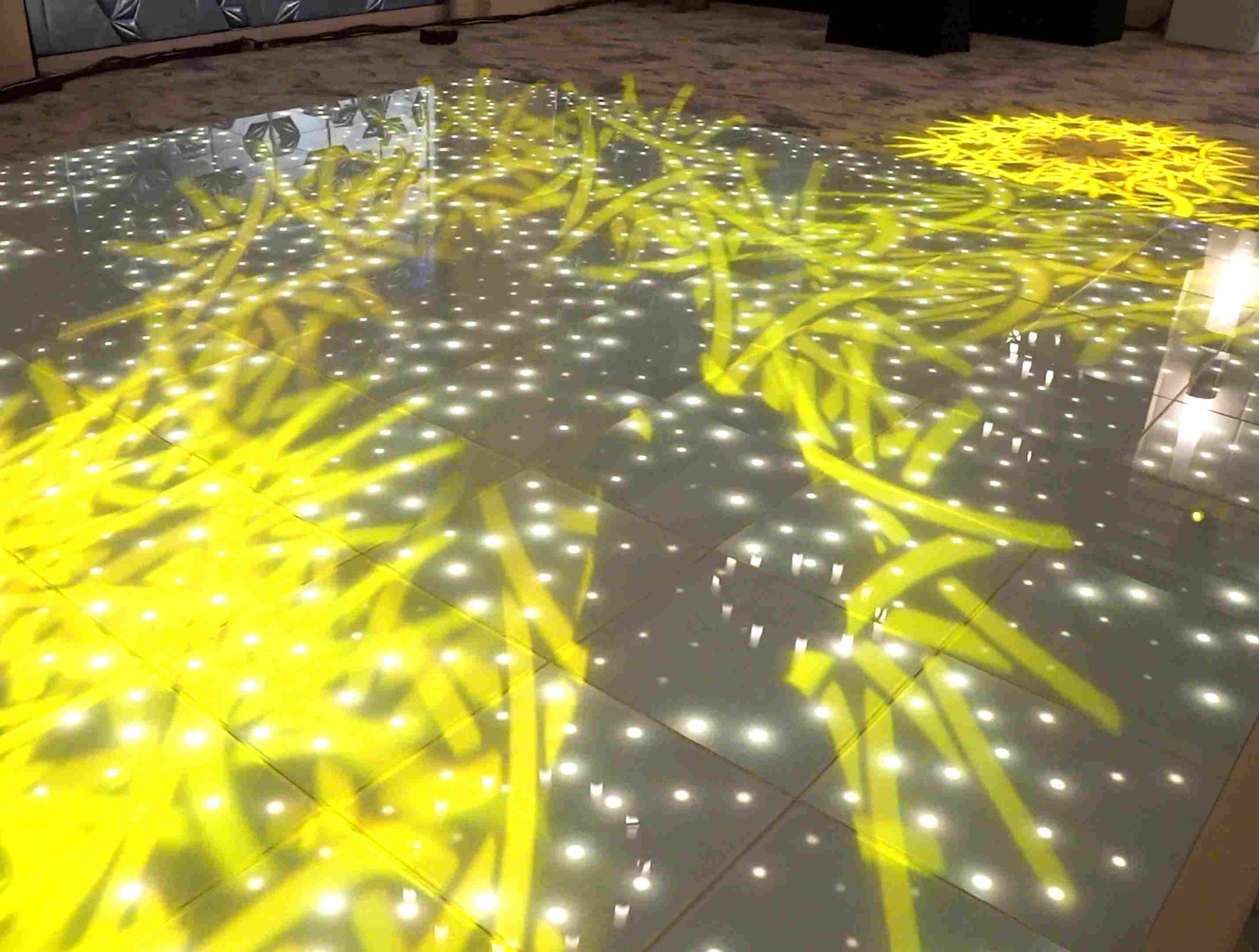 Bright yellow patterns and white dots are projected onto a glossy floor, creating a vibrant and dynamic visual effect. The atmosphere is lively.